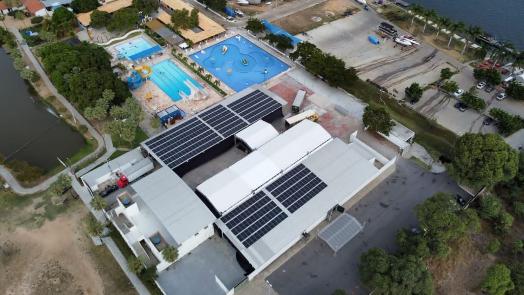 Vista aérea de um sistema fotovoltaico comercial da Senso Solar em Petrolina, com painéis solares cobrindo o telhado de um galpão industrial e céu claro ao fundo.
